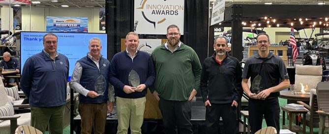 Six men stand in a row. Three of them are holding trophies.