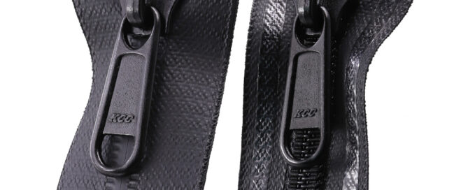 Two black zippers, with the KCC logo in a teal banner in the top-left corner.