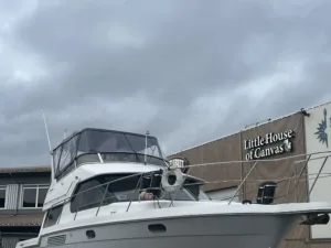 litttttt A white boat with a canopy sits in the foreground, with a building behind it displaying the sign "Little House of Canvas" under a cloudy sky.