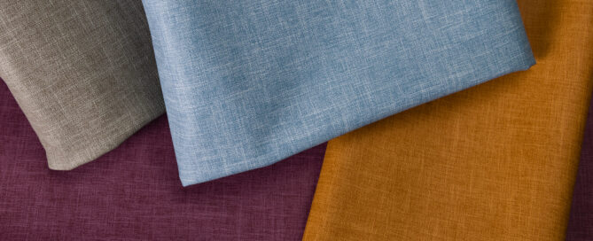 Textiles in shades of brown, light blue, orange and deep purple arranged in overlapping layers, showcasing varied textures.