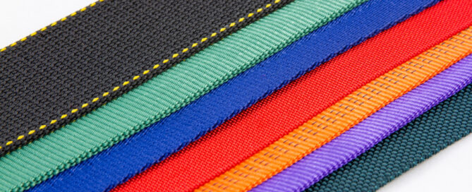 Nylon straps arranged horizontally, featuring black, green, blue, red, orange and purple textures with yellow stitching detail.