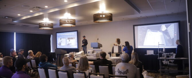 Conference attendees seated in rows watch a speaker present on stage, with a large screen displaying marine fabrication techniques.