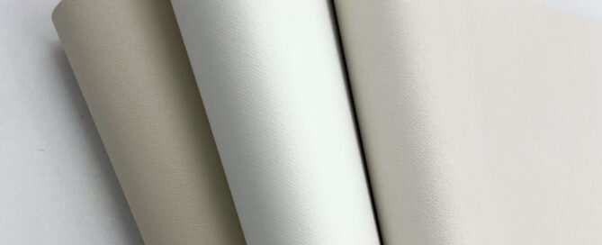 Three rolls of textured fabric in varying shades of off-white and cream, arranged slightly overlapping on a light background.