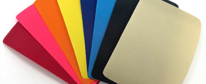 A fan of colorful fabric swatches in vibrant hues, including red, pink, orange, yellow, blue, black and beige, arranged in a gradient.