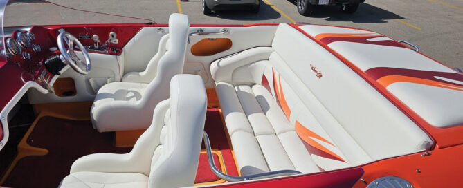 Boat interior featuring white leather seating with orange accents, a chrome steering wheel and polished dashboard gauges.